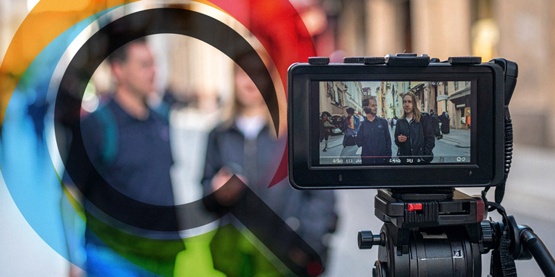 Video camera on a tripod filming two pedestrians on a city street, with colorful circular overlay in the foreground.